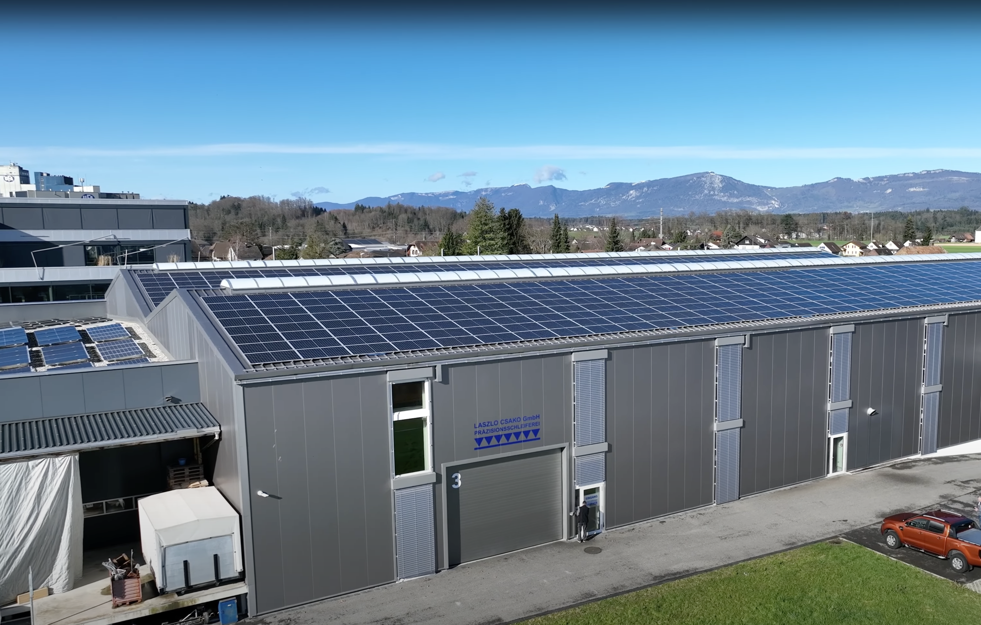 Moderne Präzisionsschleiferei in Herzogenbuchsee - Nachhaltigkeit und Präzision vereint Laszlo Csako GmbH Firmengebäude Außenansicht - Präzisionsschleiferei in Herzogenbuchsee mit Schweizer Bergpanorama und Solarpanels